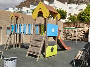 Een speelplaats met een houten glijbaan, klimconstructies en een blauwe klimmuur.