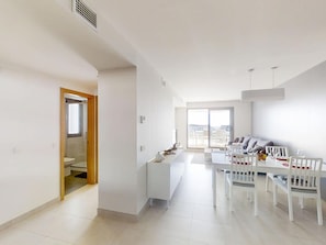 A modern living room with a dining area, a sofa, and a view through a glass door.