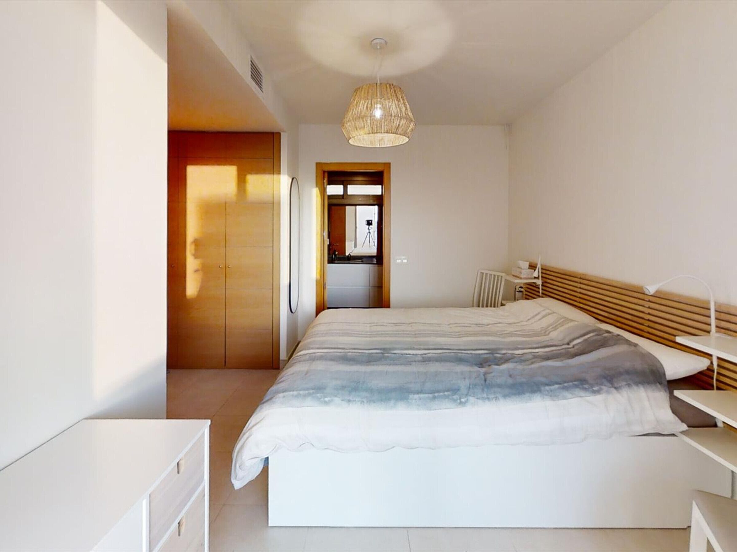 A modern bedroom with a large bed, a bedside table, a wardrobe, and a hanging light fixture.