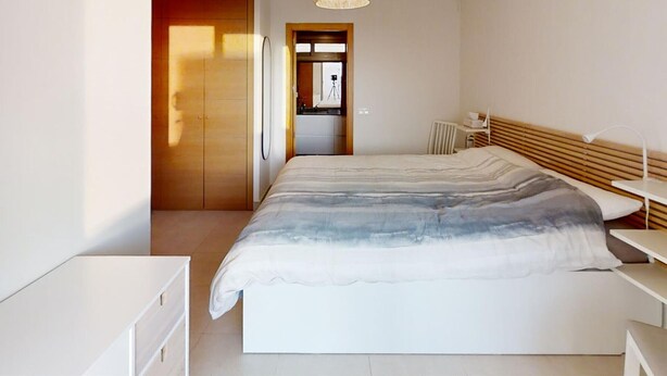 Et moderne soveværelse med en stor seng, et natbord, en garderobe og en hængende lampe.