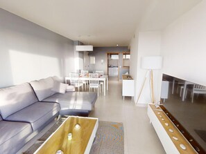 A modern living room with a sofa, coffee table, and dining area with chairs and a table. - Comfortable apartment with golf course view - 4 guests (San Juan de los Terreros)