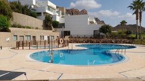 Et poolområde med to runde pools, en træterrasse og en bygning med fladt tag i baggrunden.