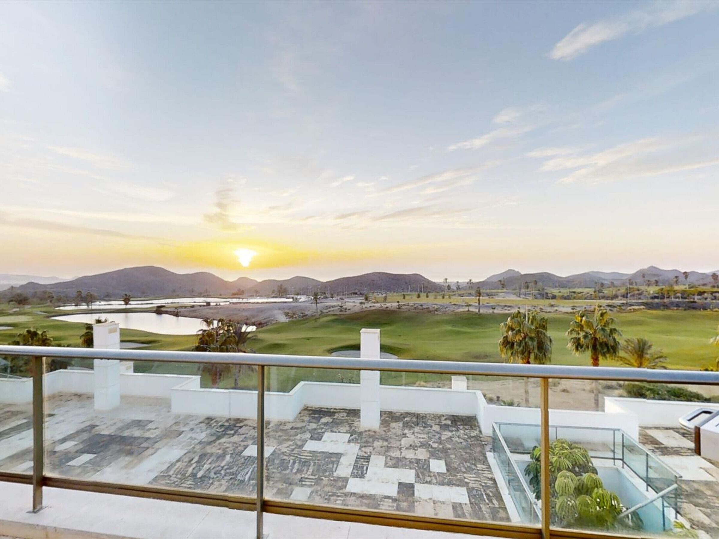 A view from a balcony overlooking a golf course with a sunset in the background.