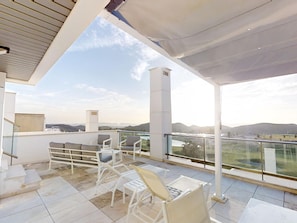 A covered outdoor seating area with white chairs and a table, overlooking a scenic landscape.