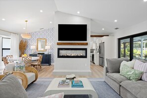 A modern living room with a fireplace, dining area, and kitchen.