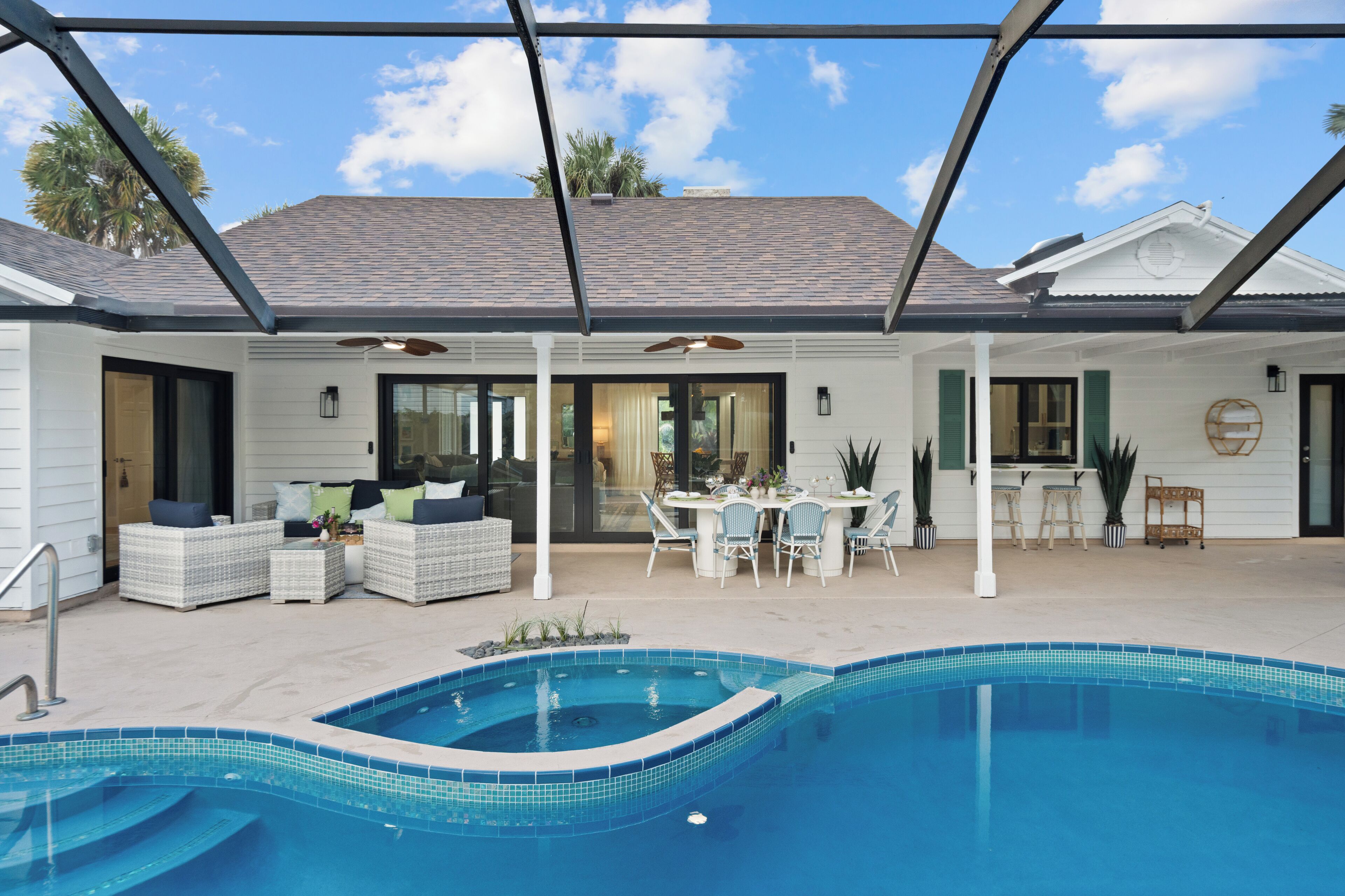 A covered outdoor area with a swimming pool, seating, and a dining table.