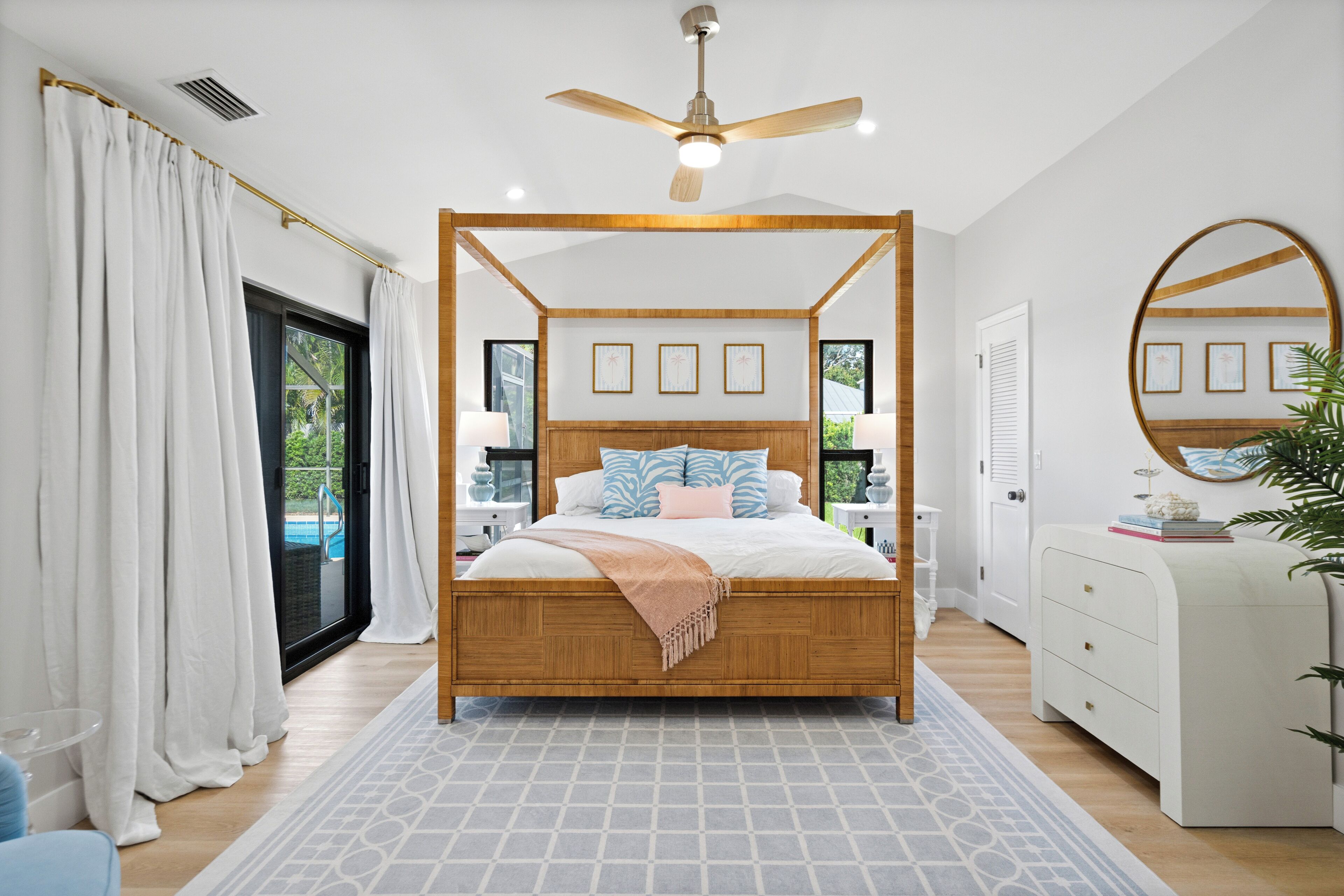 A modern bedroom with a four-poster bed, a ceiling fan, and a view of the outdoors.