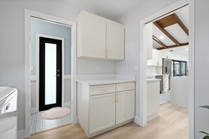 A modern kitchen with white cabinetry, a black door, and a wooden ceiling.