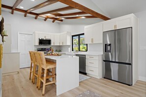A modern kitchen with white cabinetry, a stainless steel refrigerator, and a wooden dining area.
