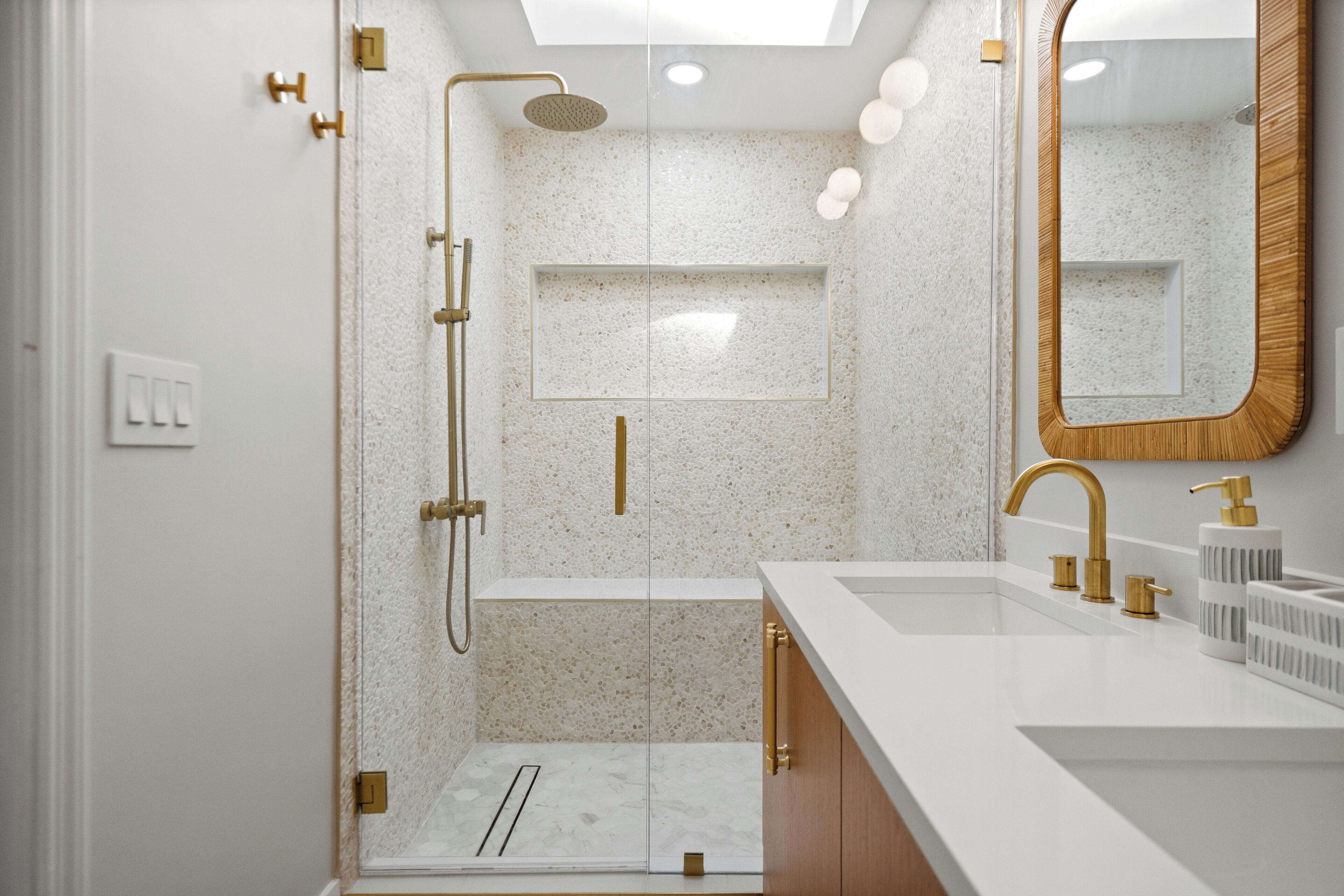 Een moderne badkamer met een douche met glazen wand, een grote spiegel en een witte wastafel met gouden details.