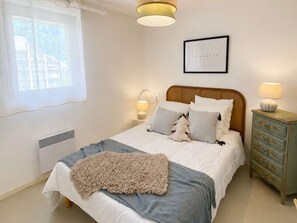 A bedroom with a bed, bedside lamps, a dresser, a window, and a wall clock. - Cozy apartment in city center - 6 guests (Saint-Lary-Soulan)