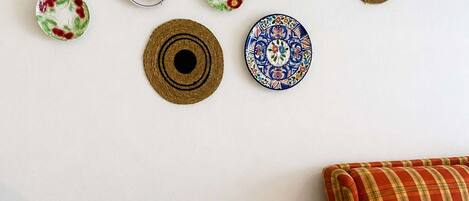 Una mesa de comedor con platos, cubiertos y una botella de vino, frente a una pared blanca decorada con platos y un sofá a cuadros.