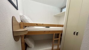 Ein Etagenbett mit Wandregal, ein kleiner Tisch und ein Kleiderschrank.