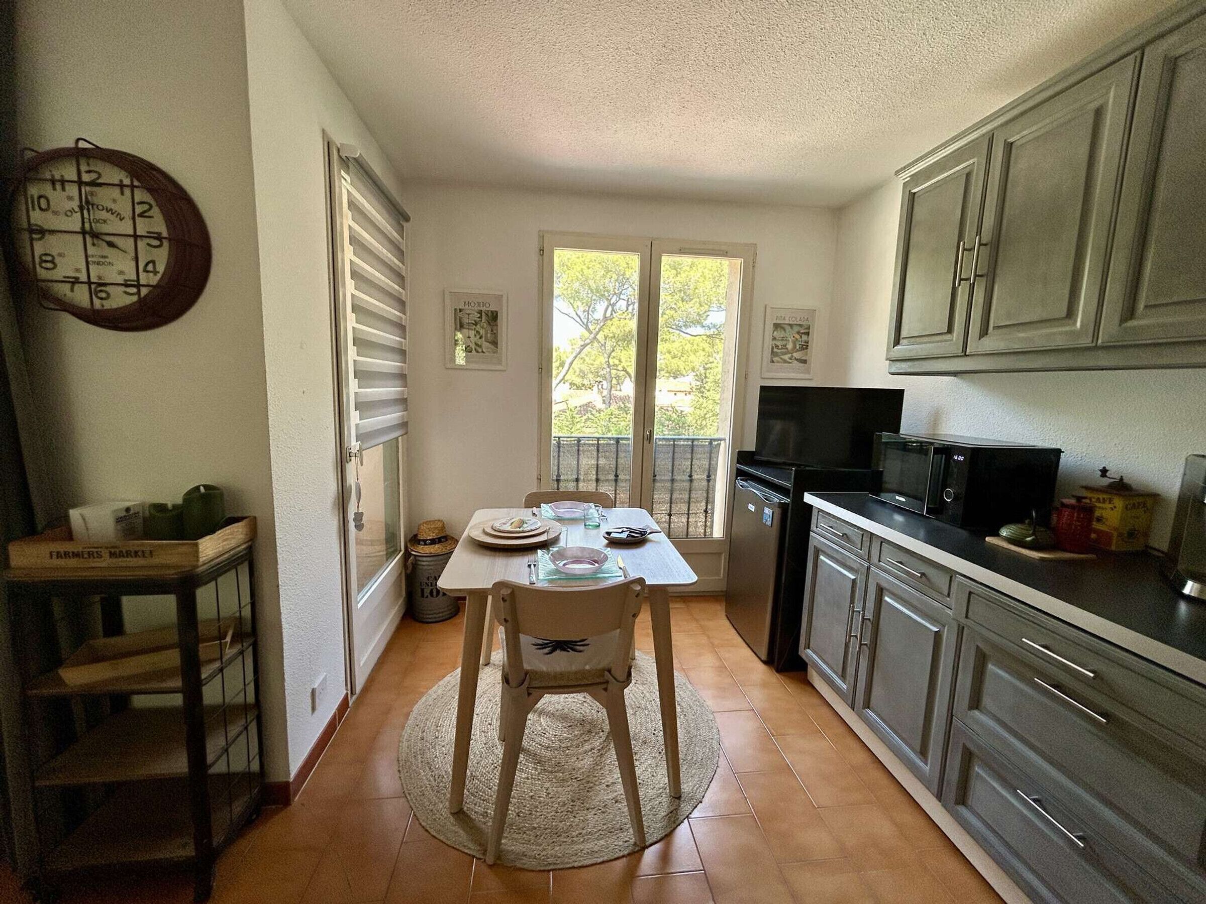 Una cocina con mesa, sillas, un reloj, armarios y un refrigerador.