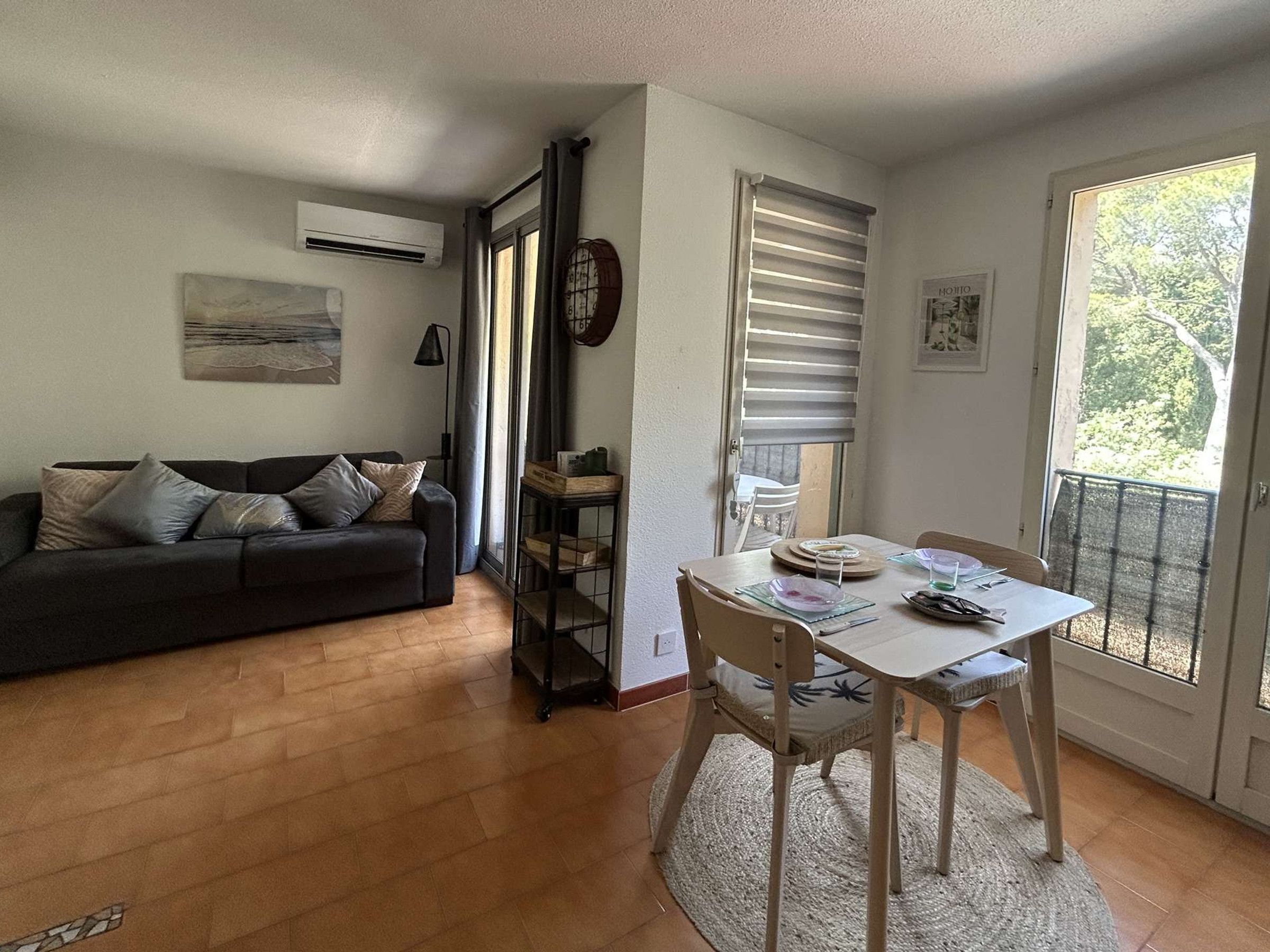 A living room with a sofa, a dining table with chairs, a small side table, and a window with blinds.