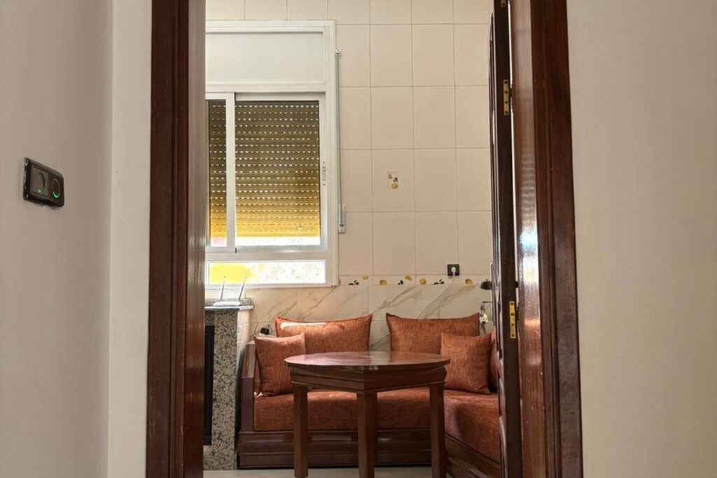 A room with a sofa and a table, a window with blinds, and a wall-mounted light switch.