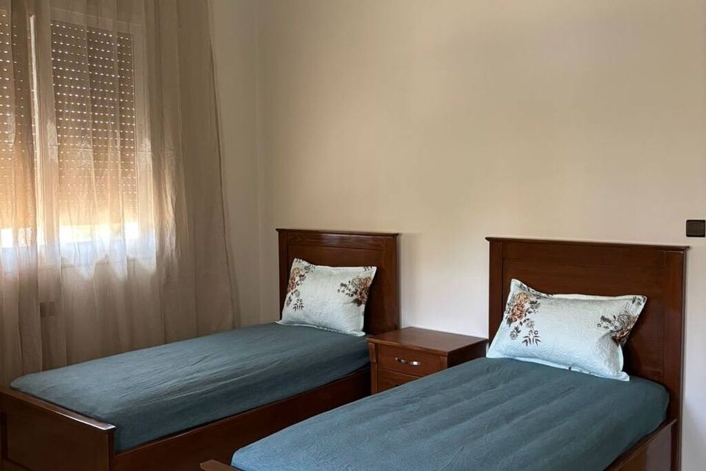 Een kamer met twee eenpersoonsbedden, elk met een houten hoofdbord en passend kussen.