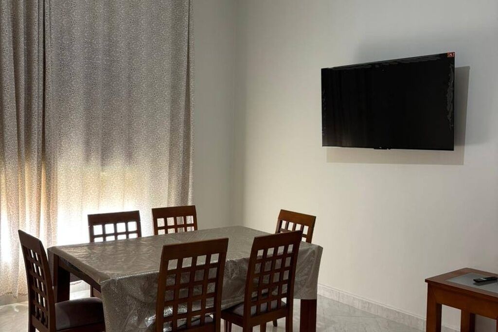 Een eethoek met een tafel, stoelen, een aan de muur bevestigde televisie en een raam met gordijnen.