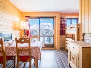Ein gemütliches Zimmer mit Holzvertäfelung, einem Esstisch mit Stühlen, einem Fernseher und Blick auf schneebedeckte Berge durch ein großes Fenster.