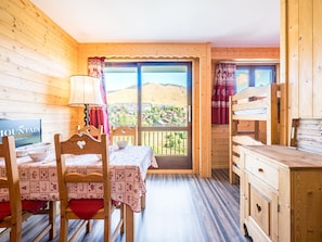 A wooden cabin with a dining area, a bed, and a view of a mountainous landscape. - Cozy studio, station view - 4 guests (La Toussuire)