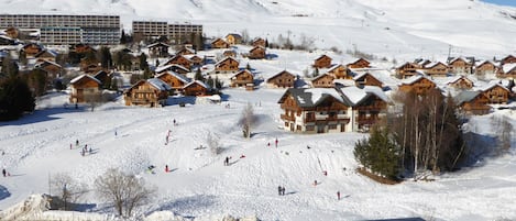 Estância de esqui coberta de neve com chalés de madeira e um teleférico ao fundo.