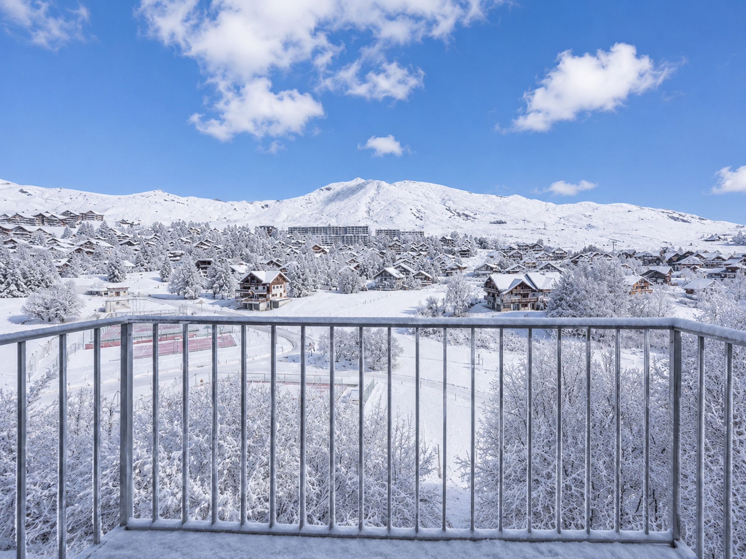 Une ville de montagne enneigée, avec des maisons traditionnelles en bois et un grand bâtiment en arrière-plan.