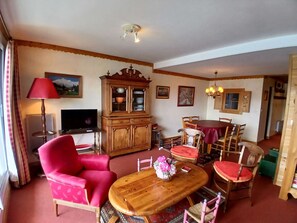 A living room with a red armchair, a wooden cabinet, a dining table with chairs, a television, and a lamp. - Spacious apartment - 8 guests, central location (Huez)