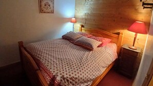 Een bed met houten frame, beddengoed met patroon en kussens, een bedlampje en een lijst met een afbeelding aan de muur.