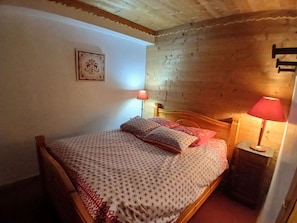 A wooden-framed bed with patterned bedding and pillows, a bedside lamp, and a framed picture on the wall. - Spacious apartment - 8 guests, central location (Huez)