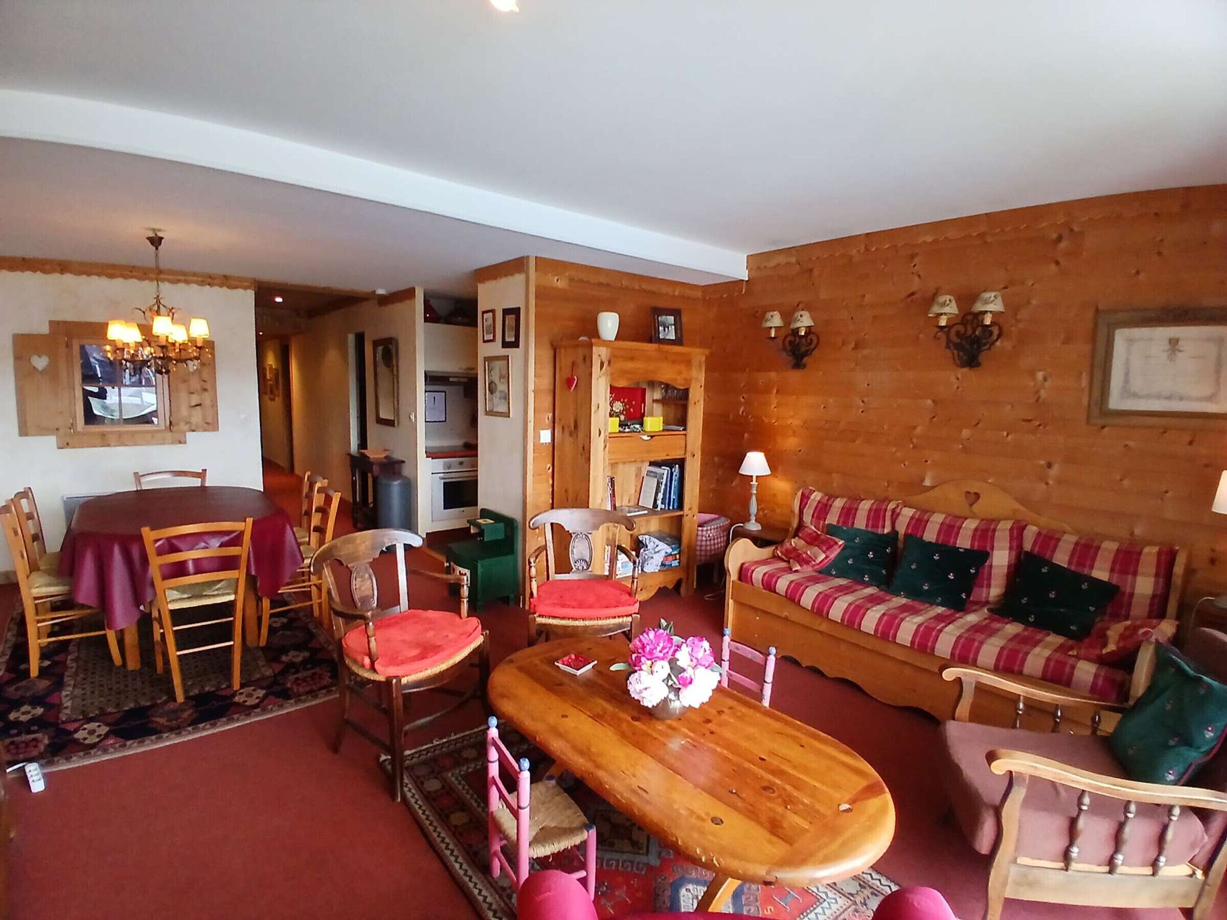 Un salon chaleureux avec un canapé en bois, une table à manger avec des chaises, une table basse en bois et un lustre.