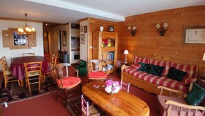 Een gezellige woonkamer met een houten bank, een eettafel met stoelen, een houten salontafel en een kroonluchter.