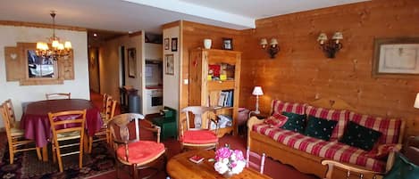 Una sala de estar acogedora con un sofá de madera, una mesa de comedor con sillas, una mesa auxiliar de madera y una lámpara de araña.