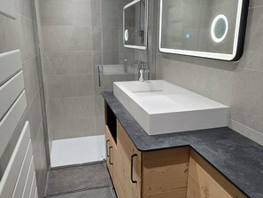 Ein modernes Badezimmer mit einem weißen Waschbecken, Holzschränken und einem Spiegel mit beleuchtetem Rahmen.