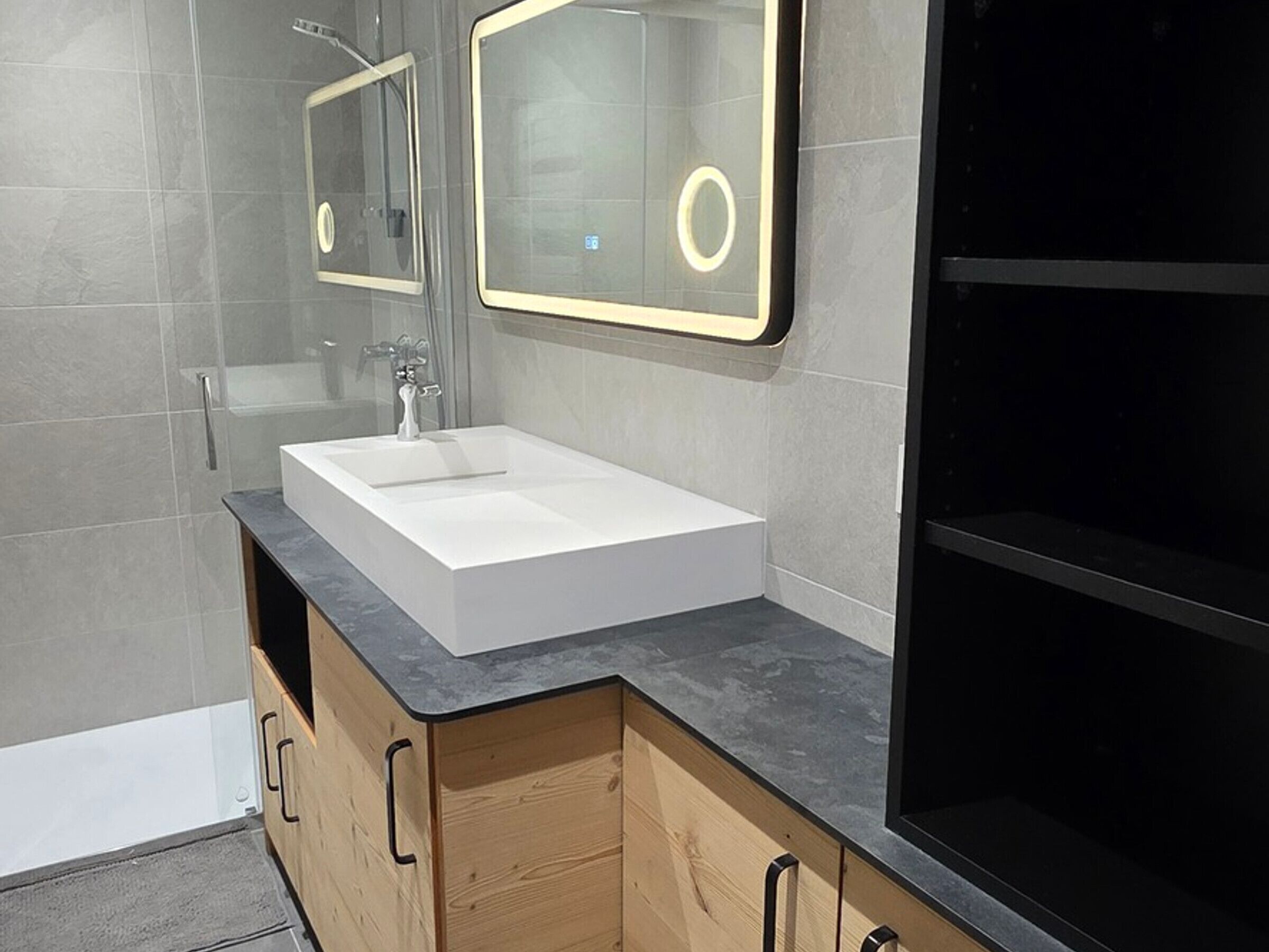 A modern bathroom with a white sink, wooden cabinets, and a large mirror with a lighted frame.