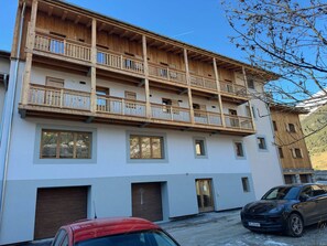 Ein mehrstöckiges Gebäude mit Balkonen, großen Fenstern und einem geparkten Auto davor.
