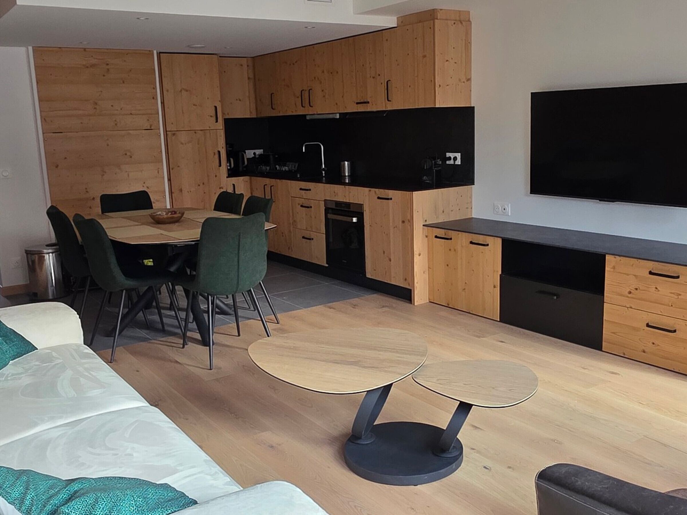 A modern kitchen with wooden cabinets, a black countertop, and a dining area with a round table and chairs.