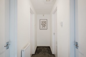 Un couloir étroit aux murs blancs, avec un radiateur sur le côté gauche et une estampe botanique encadrée accrochée au mur.