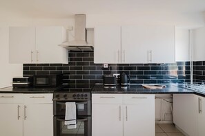 Una cucina moderna con mobili bianchi, zoccolo a mosaico nero e elettrodomestici in acciaio inossidabile.