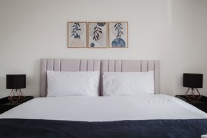 A hotel room with a bed, two bedside tables, and three wall-mounted artworks. - Modern 3 Bedroom House With WiFi (Northampton)