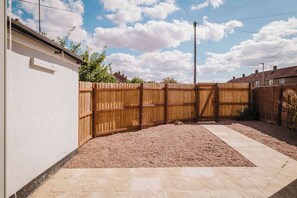 A fenced backyard with gravel and a paved walkway. - Modern 3 Bedroom House With WiFi (Northampton)