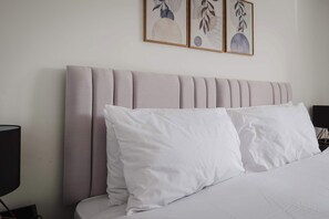Un lit avec du linge de lit blanc et une tête de lit ornée de motifs verticaux en relief.