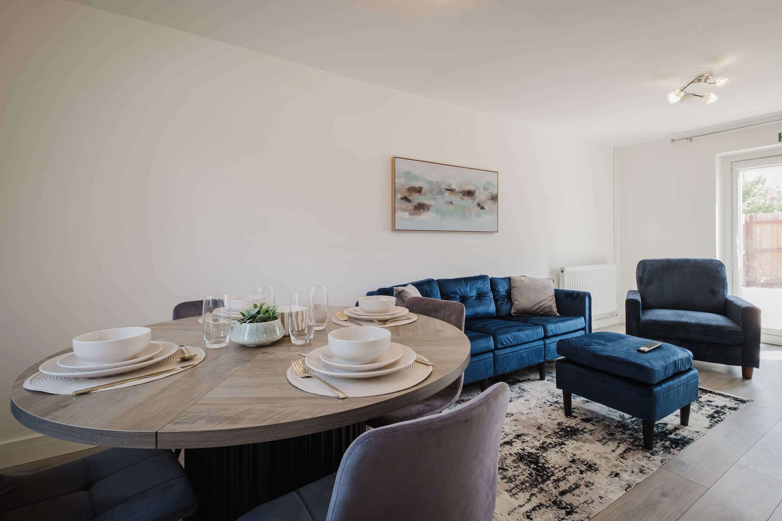 Ein stilvoller Essbereich mit einem runden Tisch, gedeckt für vier Personen, einem blauen Sofa und einem grauen Sessel.