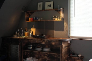 A kitchen with wooden shelves, a kettle, and various kitchen utensils.