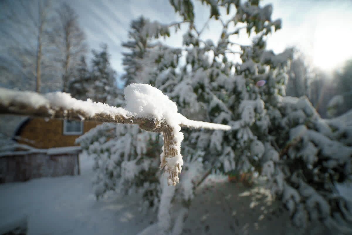Un ramo ricoperto di neve con stalattiti, uno sfondo sfocato di una casa e alberi imbiancati.