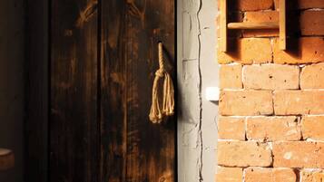 Una porta de fusta amb una tranca de metall i una corda lligada, una paret de maó amb una prestatgeria de fusta, i una vista parcial d'una habitació amb una paret blanca i una finestra.