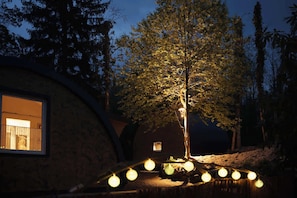 Un arbre il·luminat per llums, un edifici amb una finestra i una construcció circular.