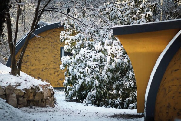 A snow-covered pathway leading to a yellow building with a curved roof, surrounded by snow-laden trees.