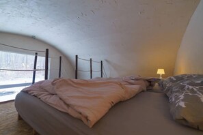 A bedroom with a bed, a lamp, and a view of the outdoors.