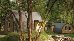 A rustic cabin with a curved roof, surrounded by trees and a stone pathway. - Point NEMO Digital Detox - Maga Capsule with Sauna (Mirsk)