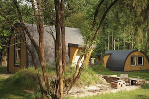 A rustic cabin with a curved roof, surrounded by trees and a stone pathway. - Point NEMO Digital Detox - Maga Capsule with Sauna (Mirsk)